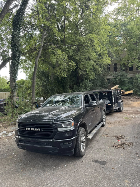A black RAM truck towing a dump trailer with debris for The Dump Bros LLC on a dirt path in Raleigh, NC.