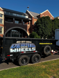 A black dump trailer with Debris On Wheels branding parked on a street in Eugene, OR.