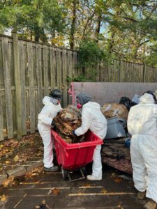 Workers in protective suits removing debris in a red cart during a restoration job by Professional Restoration in Jersey City, NJ