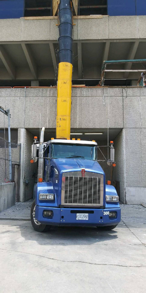 A blue semi-truck with a debris chute for construction debris removal, handled by R A Seaton Contractor Services in Rockford, IL.