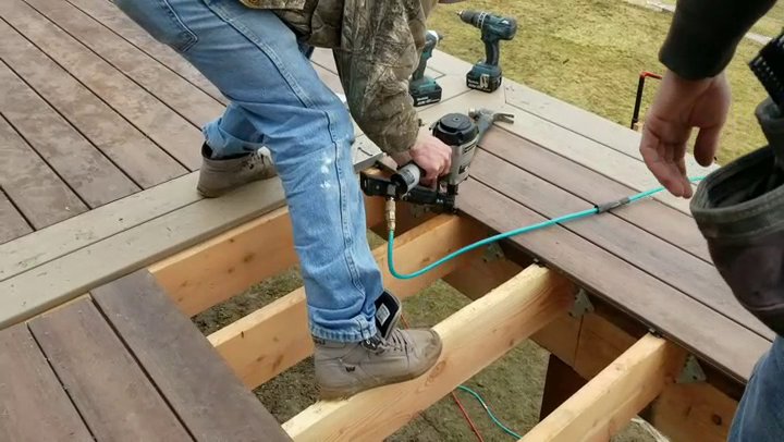 A worker installing composite deck boards with a nail gun, demonstrating craftsmanship by Ridgeline Decks in Spokane, WA.