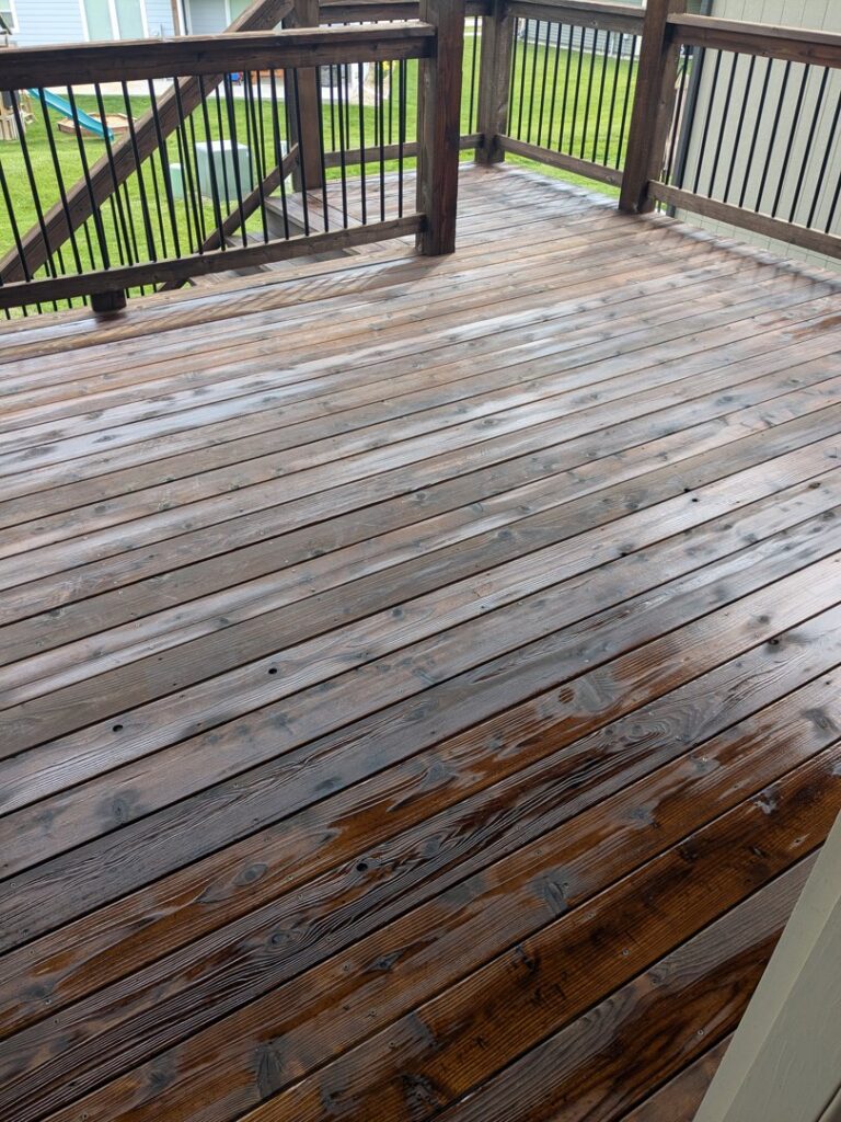 A wooden deck appearing wet, possibly after cleaning or staining, a service offered by Homefix Lawrence in Lawrence, KS.