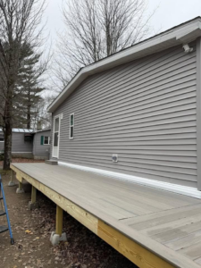 A long wooden deck under construction next to a house with new grey siding by The Finish Group in Bangor, ME.