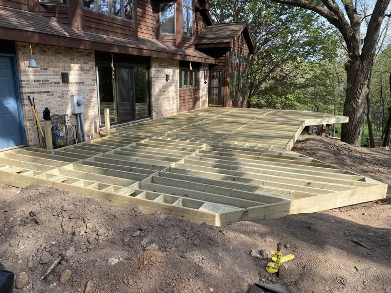 The wooden framework of a large deck under construction on a sloped property by Building Arts by Jimmy Z in Cassville, WI.