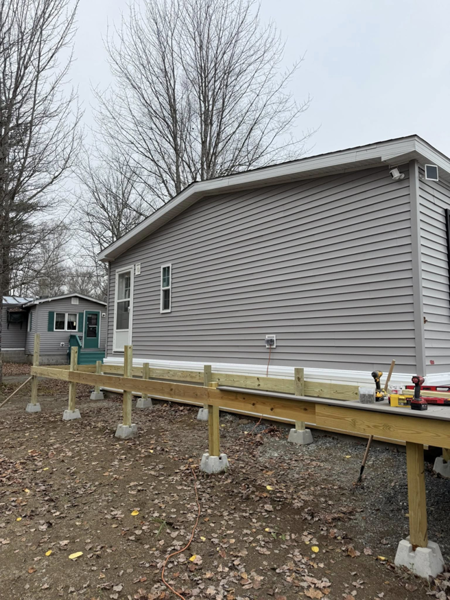 A wooden deck frame under construction next to a house, showcasing work in progress by The Finish Group in Bangor, ME.