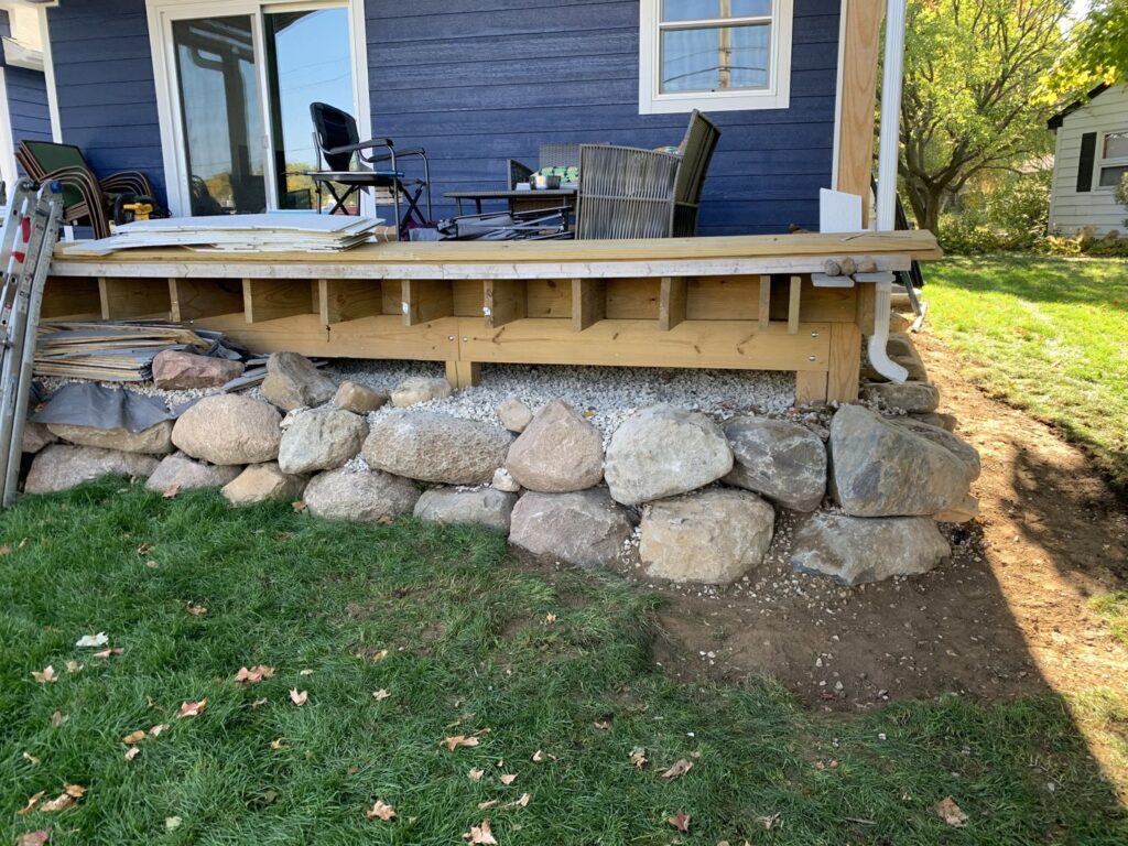 Deck framing under construction with decorative rocks at the base by S-Squared Construction in Madison, WI.