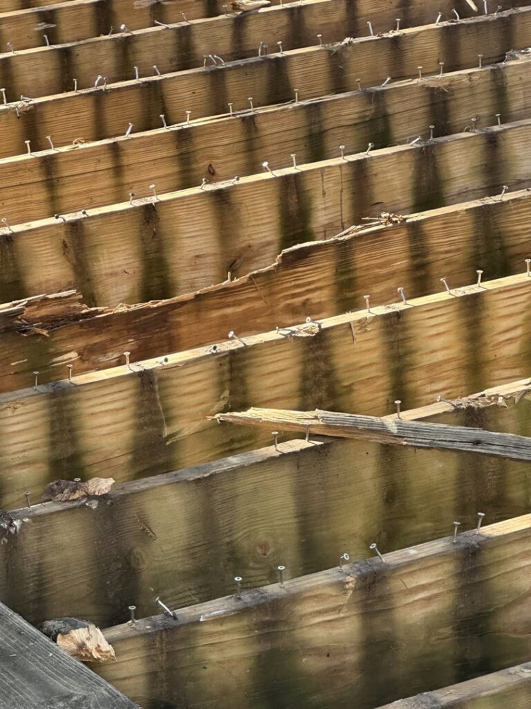 Close-up of wooden deck joists with nails, showing ongoing repair work by Jewell Services handyman in Des Moines, IA.