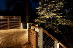 A custom-built deck with integrated lighting and modern cable railings at night by Constructive Design Group in Raleigh, NC
