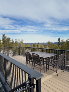 A beautiful composite deck with outdoor furniture, offering a scenic mountain forest view, installed by AG - Deck Masters in Arvada, CO.
