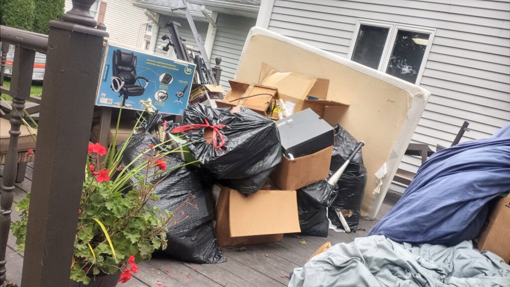 A residential deck piled high with black trash bags, cardboard boxes, and a mattress, awaiting junk removal by HAULA Junk Removal in Canton, OH.