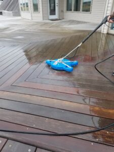 A person using a surface cleaner attachment to pressure wash a wooden deck by Amazing Handyman Services in West Fargo, ND