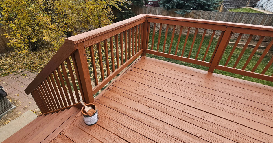 A freshly stained wooden deck with a can of stain and brush, showcasing a completed project by All Hung Up LLC in Littleton, CO.