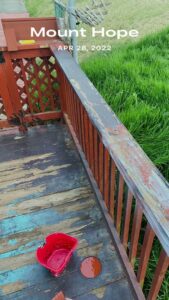A wooden deck railing showing peeling paint and a paint can, indicating a staining or repair job by In Goode Hands LLC in Beckley, WV.