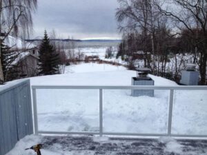 A deck with a modern glass railing installation, overlooking a snowy landscape, by Ground Up Services in Anchorage, AK.