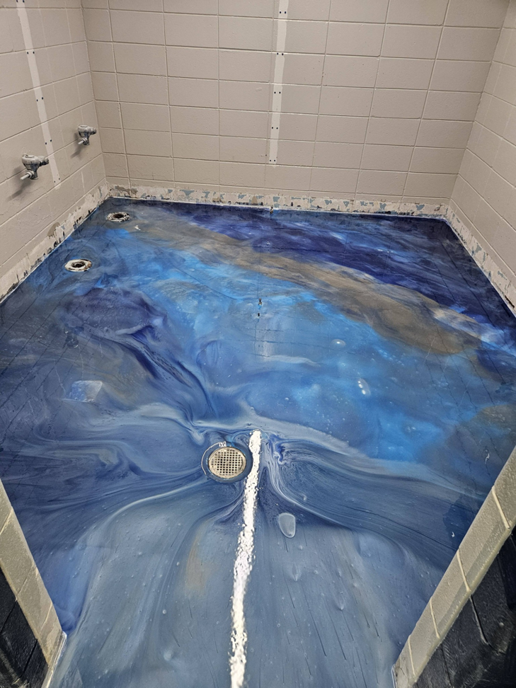 A vibrant blue decorative epoxy floor with floor drains installed by New Age Decorative Concrete in Broussard, LA.