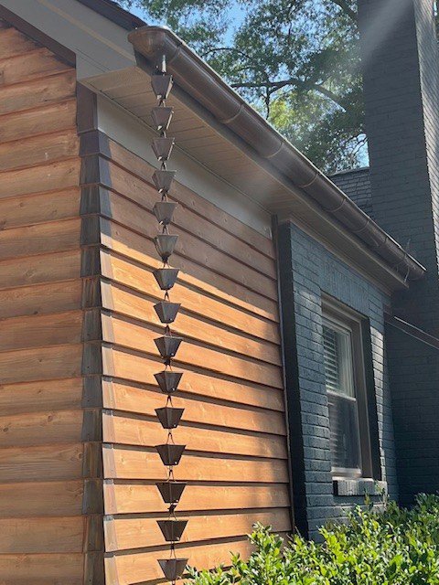 A decorative rain chain installed as a downspout alternative on a house, a service offered by Monroe Gutter Pros in Charlotte, NC.