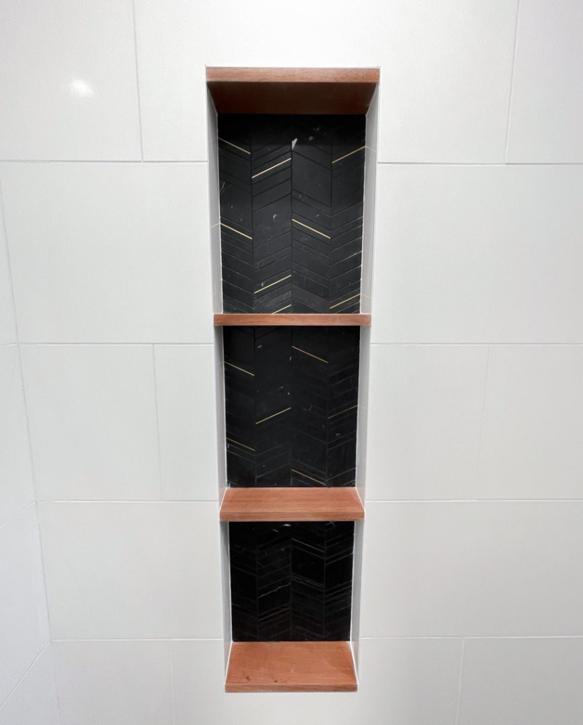 A decorative shower niche with wooden shelves and herringbone tile by Clean Cut Tile LLC in St. Louis, MO.