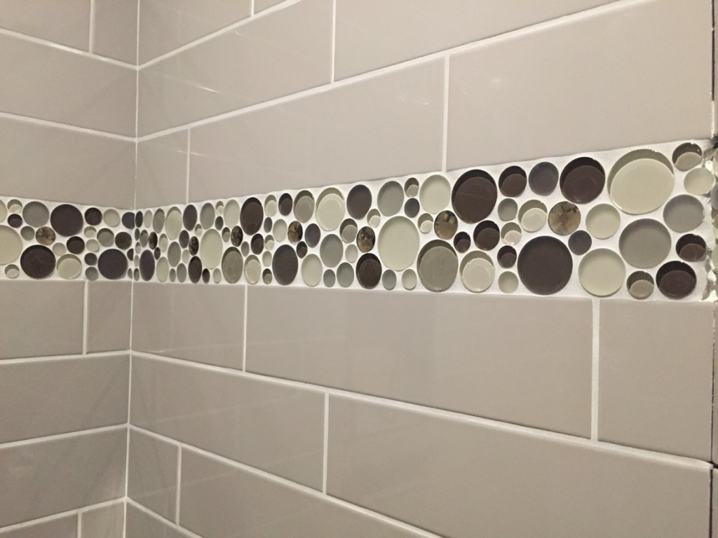 Close-up of a beautifully tiled wall with a decorative mosaic strip by Fueled Up Flooring- Justin Watruba in Eau Claire, WI.