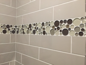 Close-up of a beautifully tiled wall with a decorative mosaic strip by Fueled Up Flooring- Justin Watruba in Eau Claire, WI.