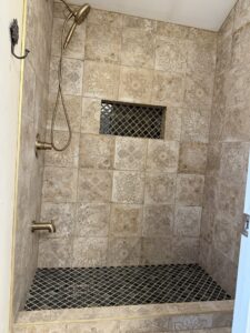 A beautifully tiled shower with decorative patterned wall tiles and bronze fixtures by Goubar Tile And More in Raleigh, NC.