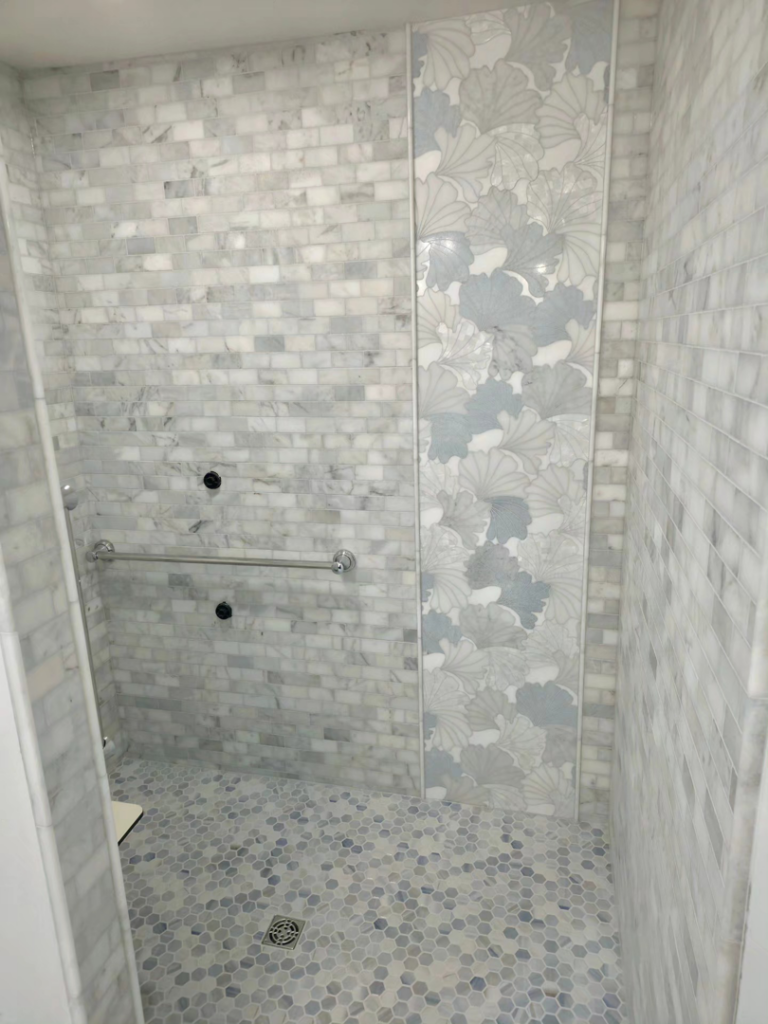 A decorative tiled shower featuring a leaf pattern and grab bar installed by Tyler the Tiler in Jefferson, WI.