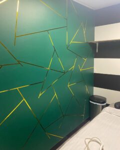 A green wall with a modern gold geometric design, a decorative painting service by In Goode Hands LLC in Beckley, WV.