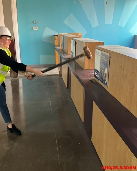 A worker in a hard hat and safety vest demolishing a wooden counter with a sledgehammer for Ringenberg Construction, LLC in Virginia Beach, VA