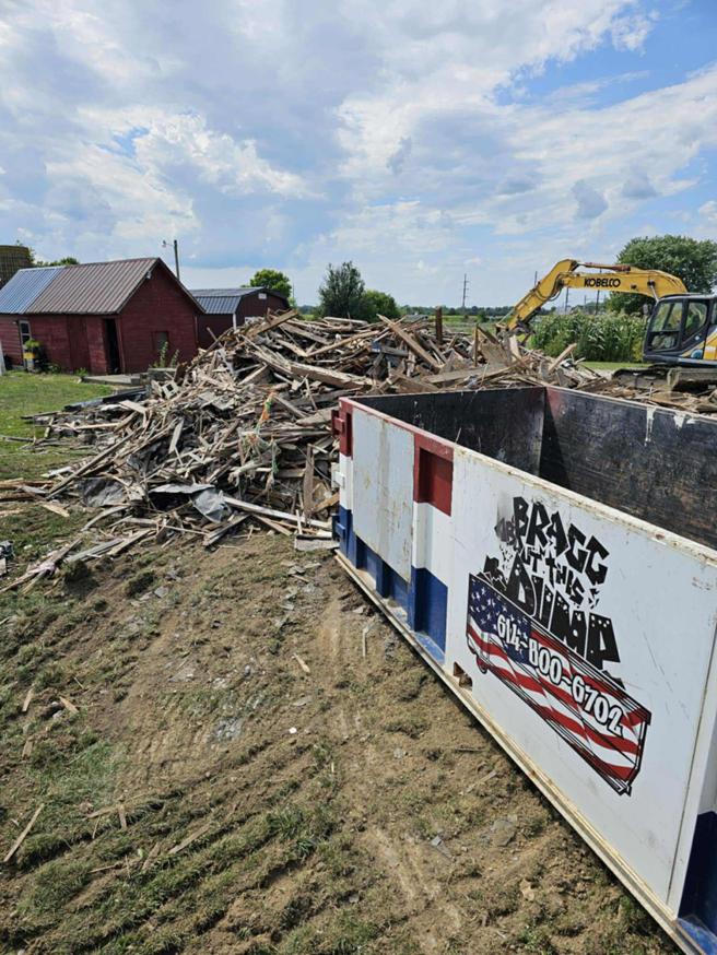 A pile of demolition debris next to a Bragg About This Dump roll-off dumpster with an excavator in Columbus, OH.