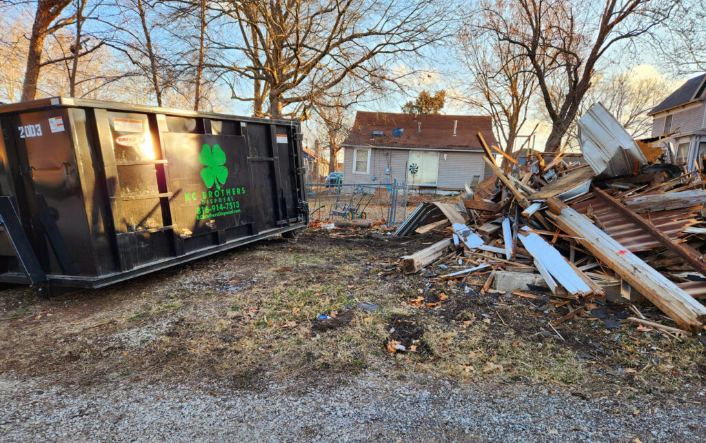 A KC Brothers Disposal dumpster positioned next to a large pile of demolition debris for removal in Kansas City, MO.
