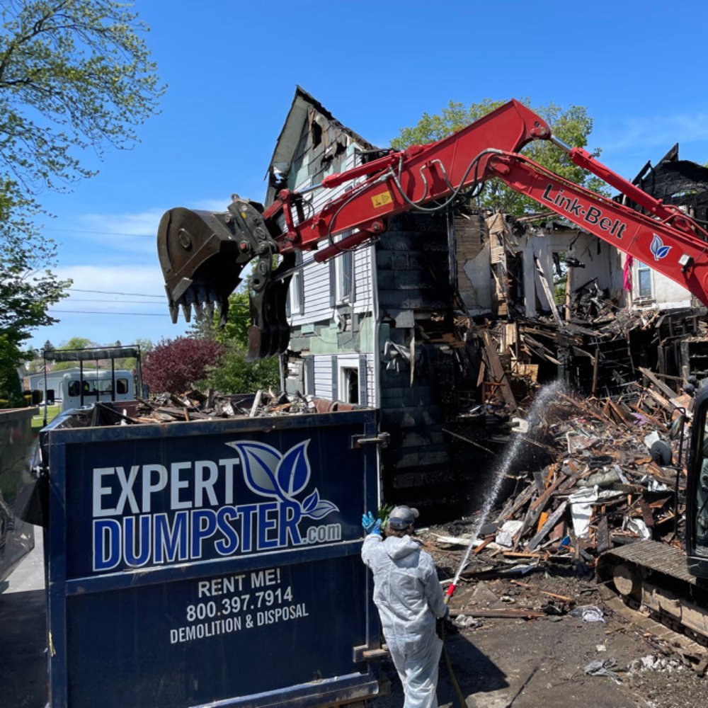 An excavator loading demolition debris into an Expert Dumpster roll-off container at a job site in Rochester, NY.