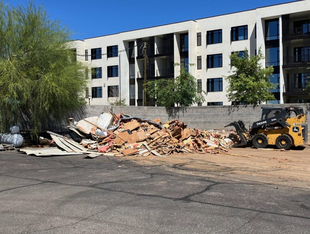 A large pile of demolition debris being cleared by a skid steer loader, handled by CzechList Junk Removal in Scottsdale, AZ.