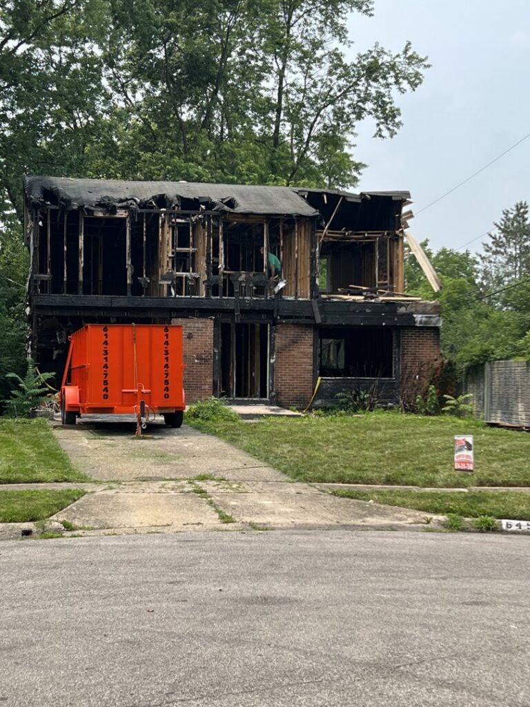 A Crazy Larry's Dumpster Rental trailer collecting demolition debris from a partially demolished house in Columbus, OH.