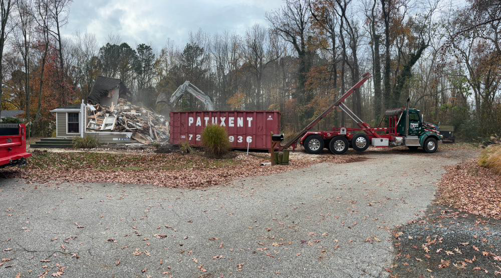 A Patuxent Roll-Off truck and dumpster at a house demolition site for debris removal in Crofton, MD