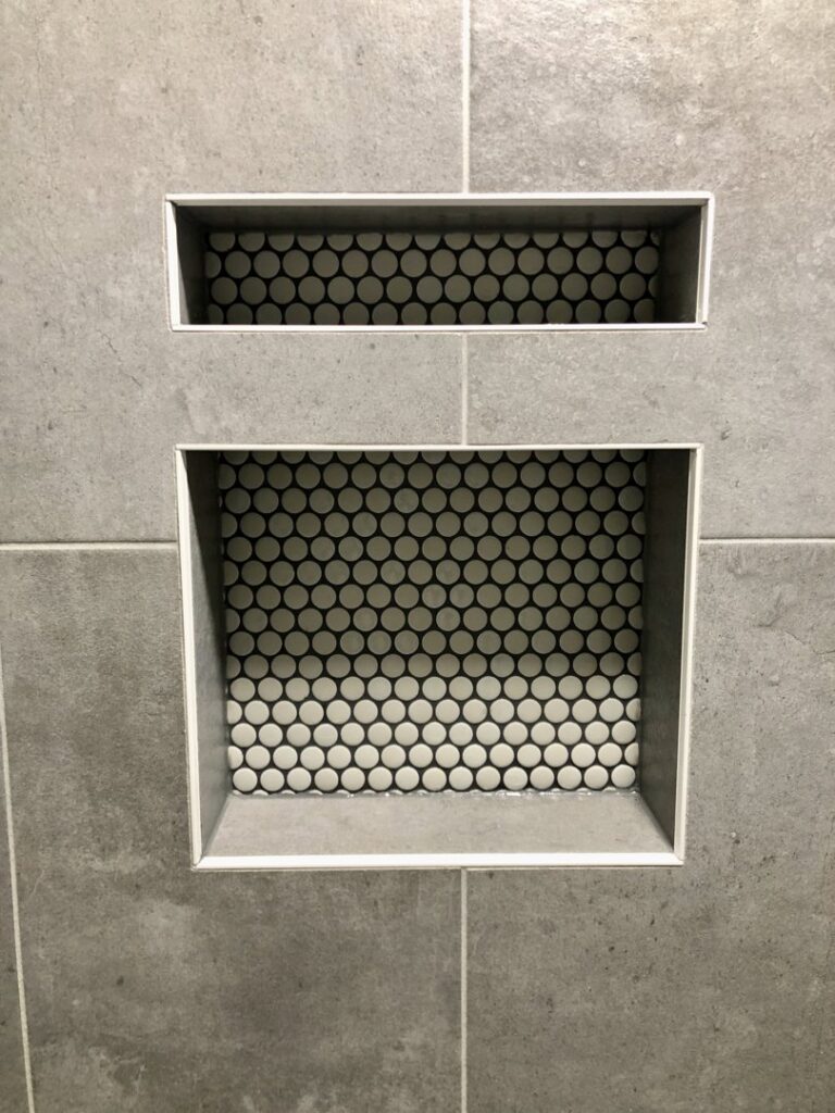 Detailed view of two mosaic-backed shower niches within grey tiled walls, showcasing craftsmanship by Tile Jawn in Philadelphia, PA.