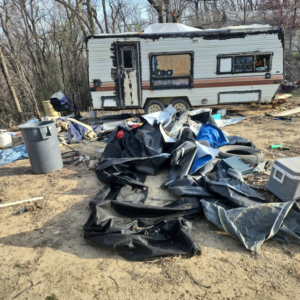 An old, dilapidated travel trailer surrounded by piles of trash and debris, showing a junk removal job by Siouxland Junk Removal in Sioux City, IA.