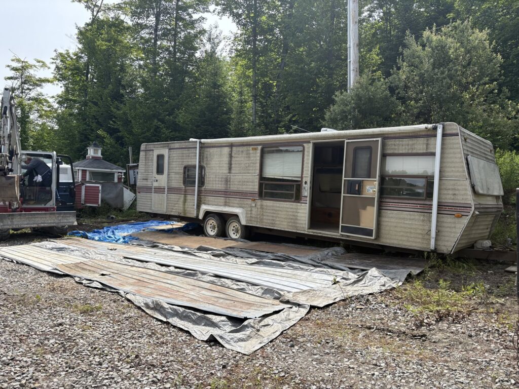 A dilapidated trailer in a field, representing a removal project for Tiny's Trash & Hauling Service L.L.C in Williamstown, VT