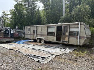 A dilapidated trailer in a field, representing a removal project for Tiny's Trash & Hauling Service L.L.C in Williamstown, VT