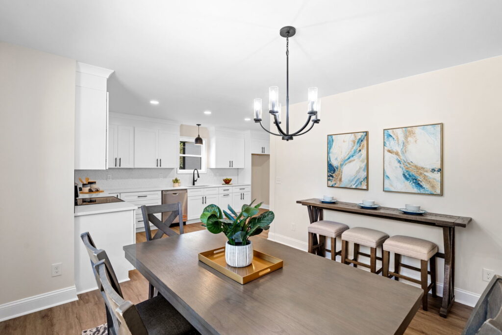 A dining room with a new chandelier and kitchen in the background by Heroic Builders LLC in Greenville, SC.