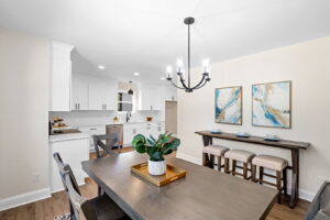 A dining room with a new chandelier and kitchen in the background by Heroic Builders LLC in Greenville, SC.