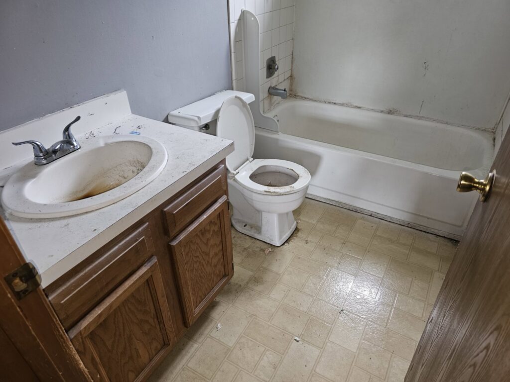 A dirty bathroom with a grimy sink, toilet, and bathtub, indicating a cleanout service by T&G Dumping in Lorain, OH.