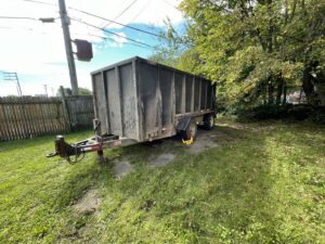 A dirty dump trailer from The Dump Town parked in a grassy area, used for junk removal in Detroit, MI.