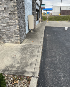 A dirty exterior sidewalk next to a stone building, an 'before' shot for cleaning services by A 2 Z Home Services - Fairmont WV.