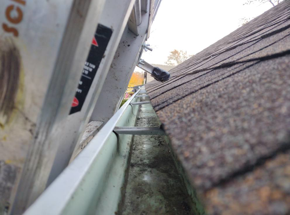 A dirty gutter and roofline viewed from a ladder, highlighting the need for gutter cleaning services from Schu Can Do 2-Property Services LLC in Warren, MI.