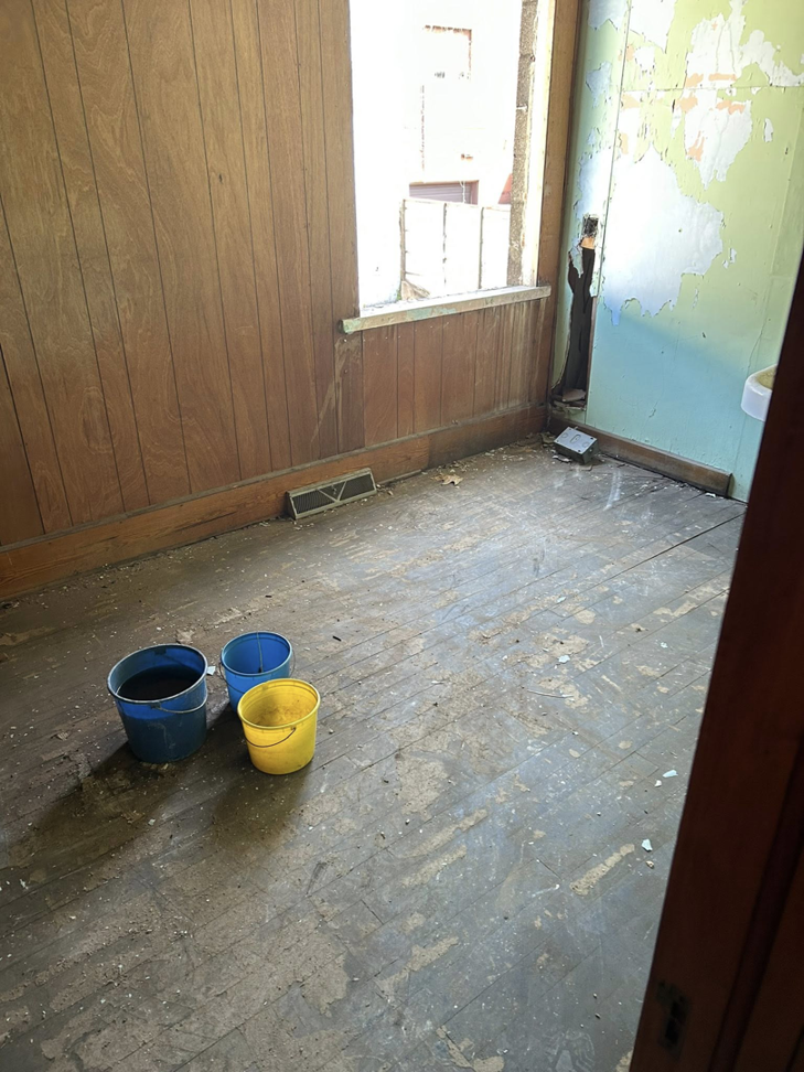 A dirty room with colorful buckets on the floor, indicating a cleanup job by County Line Junk Removal in Saint Albans, WV.