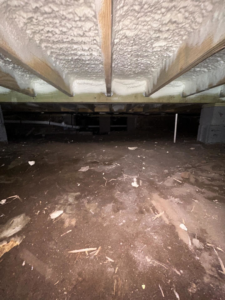 A dirty, unencapsulated crawlspace with exposed dirt and existing spray foam insulation before work by Palmetto Crawlspace in Mount Pleasant, SC.