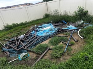 Disassembled above-ground pool parts, including the liner and frame pieces, along with other debris in a grassy backyard, ready for removal by Junk-O-Haulics in Westmoreland, TN.
