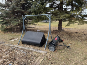 Disassembled swing set frame, lawn sweeper, and other debris on the ground, awaiting junk removal by Quality Rent & Removal in Minot, ND.