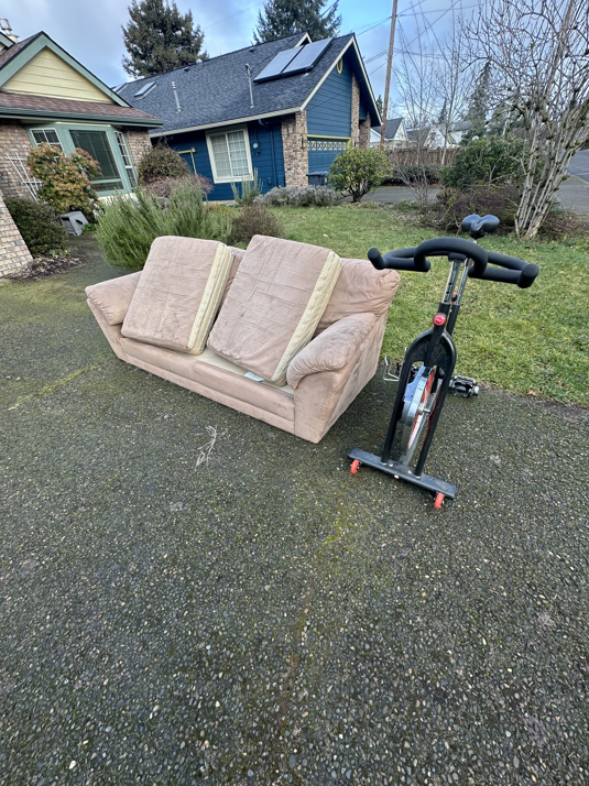 A discarded couch and exercise bike on a driveway, ready for pickup by The Recyclers, LLC Junk Removal in Springfield, OR.