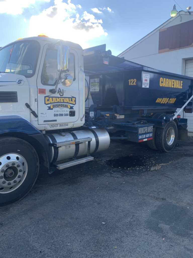 An AJ Carnevale Disposal truck with a blue dumpster parked in a commercial area in Hamilton, NJ