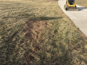 Disturbed ground with a skid steer in the background, showing the aftermath of stump removal by Farm Services in Scottown, OH.